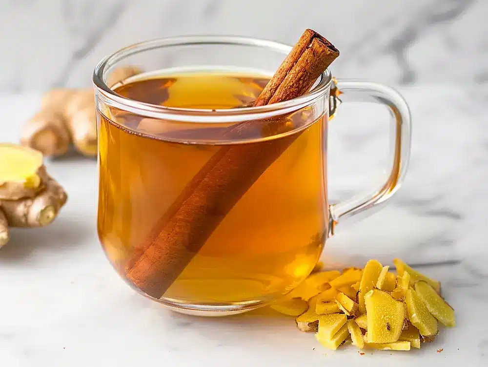 Ginger cinnamon tea for weight loss in glass mug with cinnamon stick and fresh ginger on marble countertop