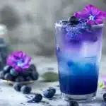 Butterfly pea tea in glass with fresh blueberries, vibrant blue herbal drink