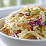 Creamy apple cider vinegar coleslaw dressing on shredded cabbage in a white bowl.