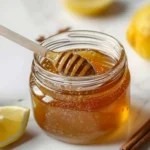 Ben carson honey recipe in open glass jar showing warm amber cinnamon honey blend with honey dipper and lemon on white marble