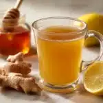 dr gupta honey recipe in clear ceramic mug with raw honey jar fresh lemon and ginger on white marble