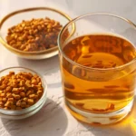 fenugreek water for weight loss in a clear glass with soaked fenugreek seeds on white marble