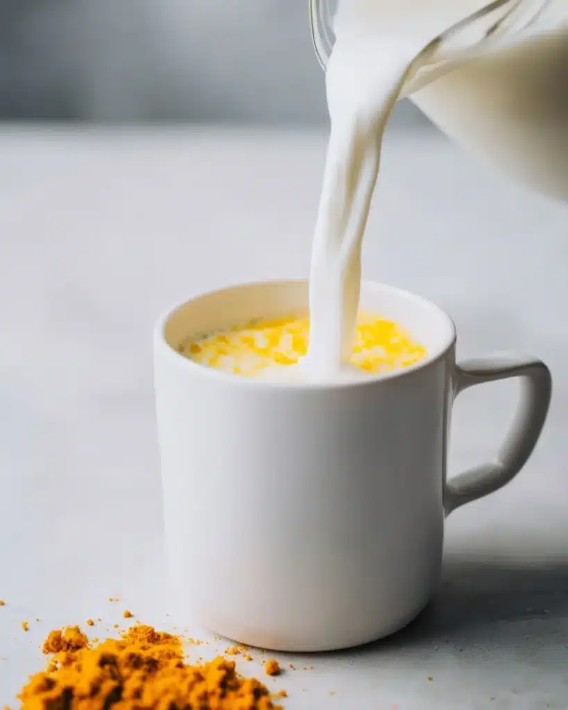 warm milk being poured into turmeric with piperine paste in a white mug