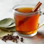 Bay leaf clove cinnamon tea in glass mug on white marble