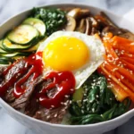 Authentic bibimbap recipe in white ceramic bowl with seasoned vegetables, marinated beef, fried egg, and gochujang sauce