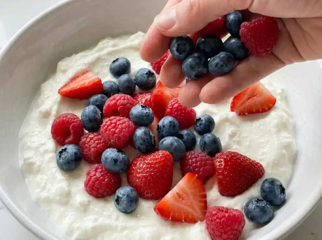 fresh blueberries raspberries strawberries scattered onto white greek yogurt in ceramic bowl dr phil low sugar recipe