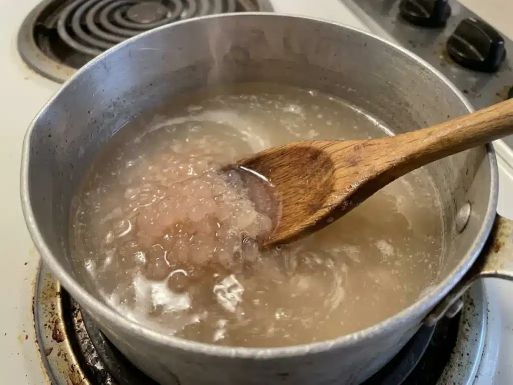 wooden spoon stirring bloomed gelatin dissolving into warm water in small saucepan for dr william li gelatin recipe weight loss