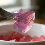 fork spearing single wobbly pink gelatin cube from white bowl showing soft jiggly texture of dr william li gelatin recipe for weight loss