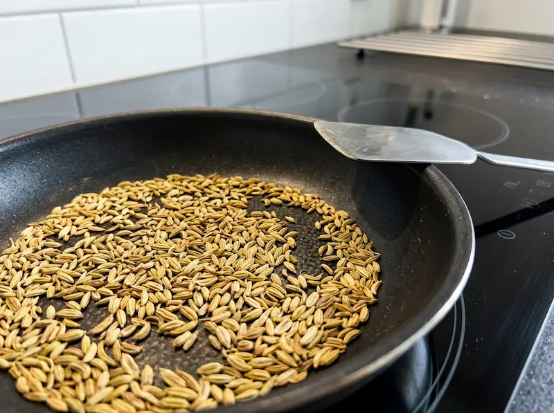 Toasting Fennel Seeds in a Pan whole fennel seeds toasting in a dry stainless steel pan on a modern induction stove