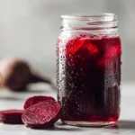 Hero image of deep ruby red beet kvass recipe in clear mason jar on white marble surface