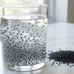 Sabja seeds soaked in clear glass of cold water with gel coating visible on white marble
