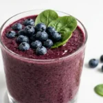 berry spinach smoothie in a clear glass with fresh blueberries and spinach