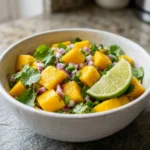 Close-up of chunky mango salsa in a white bowl with cilantro and lime