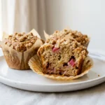 Close-up of bakery-style rhubarb muffins with crumb topping on a white plate