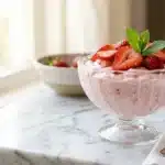 Extreme close-up of airy, pastel pink zero sugar jello Greek yogurt fluff filling a glass bowl.