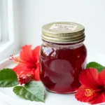 hibiscus jelly in a glass jar with red hibiscus flowers