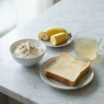 Seven easy to digest recipes for Wegovy nausea arranged on a white marble surface including a ginger chicken rice bowl and plain toast