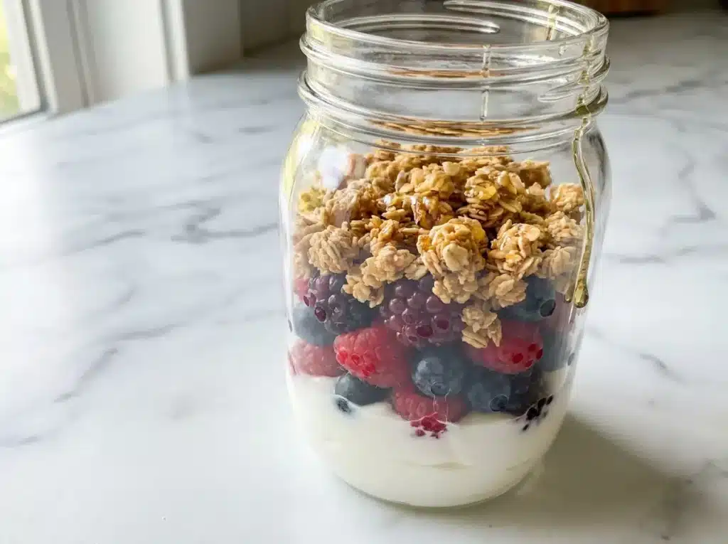 7 High Protein Meal Prep Recipes That Hit 50g of Protein Per Container 7 Greek yogurt protein parfait with mixed berries, plain granola, and a honey drizzle layered in a wide-mouth mason jar on white marble
