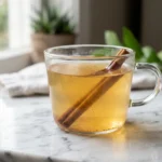 Warm honey and cinnamon drink in a clear glass cup on a white surface.